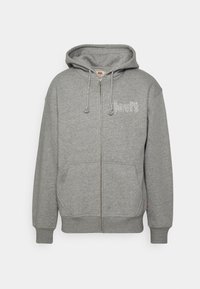 Sudadera gris con cremallera hecha de tejido suave, que cuenta con un bolsillo canguro, capucha con cordón y un logo en blanco en la parte frontal. Puños y dobladillo acanalados.