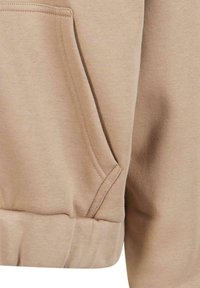 Hoodie beige avec une poche kangourou, texture douce, ourlet côtelé et poignets. Le tissu est lisse avec un design simple et classique.