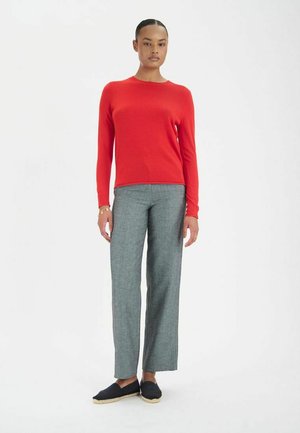Pull ajusté rouge, pantalon large gris, et espadrilles noires. Texture lisse, col rond, manches longues, détails minimaux.