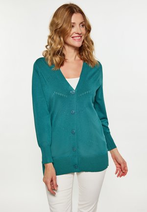 Cardigan tricotat teal, cu guler în v, mâneci lungi și detalii decorative cu motive deschise. Are cinci nasturi și o margine dreaptă.