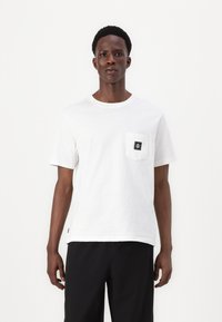 White cotton t-shirt featuring a round neck, short sleeves, and a left chest pocket with a black logo patch. Simple, straight cut design.