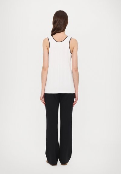 White tank top with black trim, paired with loose black trousers. The fabric appears smooth with a relaxed fit. No notable patterns.