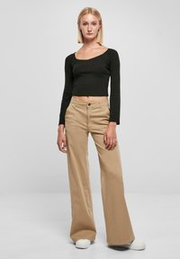 Zwarte langmouw cropped top gecombineerd met beige wijde broek en witte sneakers. Glad materiaal, eenvoudig ontwerp en een natuurlijke pasvorm.