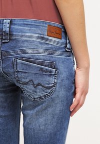 Nära bild av en person som bär blå Pepe Jeans med en vikt tygbit i bakfickan och en brun läderetikett på midjebandet.