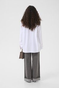 Λευκό πουκάμισο με κουμπιά και μακριά μανίκια, συνδυασμένο με φαρδιά γκρι τζιν με διπλωμένα μανσέτα. Το άτομο κρατά μια μικρή καφέ τσάντα.