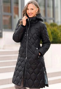 Schwarze gesteppte Parka mit Kapuze, ausgestattet mit einem Reißverschluss, Zugkordel, Seitentaschen und einer strukturierten, gemusterten Oberfläche.