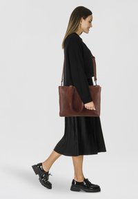 Borsa tote in pelle marrone con doppi manici e tracolla regolabile. Texture liscia, forma rettangolare e chiusura con zip.