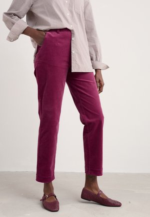 Magenta corduroy trousers with a straight cut, side pockets, and matching woven flats; paired with a striped button-up shirt.