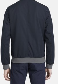 Námořnická bombardovací bunda s hladkým povrchem, ribovanými šedými manžetami a lemem a jednoduchým designem na zádech. Bez viditelných grafik nebo log.