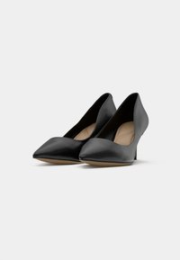 Décolleté punta nera in pelle con tacco basso, caratterizzate da una texture liscia e un design minimalista. L'interno è di un colore neutro chiaro.