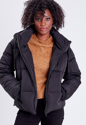 Doudoune noire avec un col haut, fermeture éclair et poignets élastiques, associée à un pull en tricot orange avec un motif texturé.