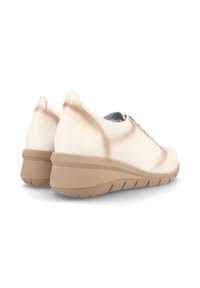 Zapatillas de deporte beige claro con un acabado suave, que cuentan con una media suela acolchada, una suela exterior de goma texturizada y un diseño de punta redondeada.