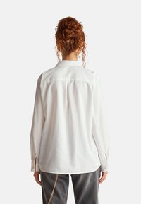 Camicia bianca a manica lunga con una sottile texture, taglio dritto e colletto classico. Caratterizzata da polsini con bottoni e orlo curvo.