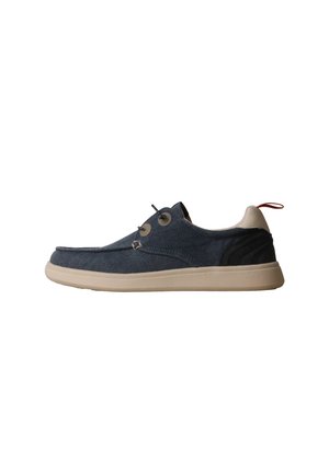 Chaussure basse décontractée avec tige en denim, semelle beige, patch noir au talon, col beige et languette rouge sur fond blanc.