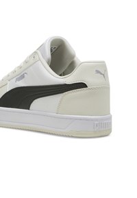 Zapatilla blanca con una franja negra de Puma, parte superior de cuero liso, cuello acolchado, suela de goma y logo en relieve en el talón.