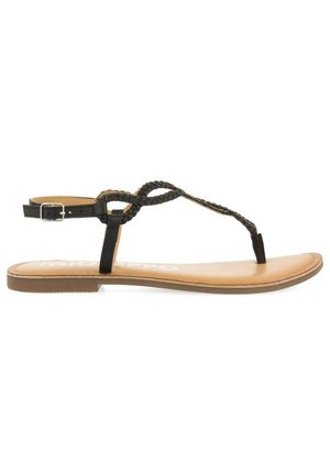 Sandalia plana negra de material sintético con una tira de dedo trenzada y hebilla ajustable en el tobillo. Plantilla en color beige claro con suela exterior marrón texturizada.