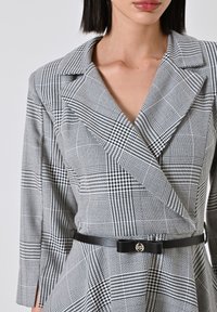Geruite blazer in zwart-witte stof, met een dubbelbreasted ontwerp, opvallende revers en een zwarte riem met een metalen logo sluiting.