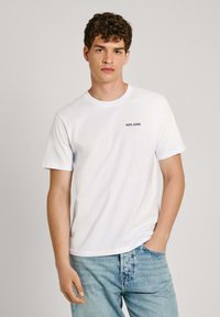 Camiseta de algodón blanca de manga corta y cuello redondo, con un pequeño logo de "PEPE JEANS" en el lado izquierdo del pecho, combinada con unos vaqueros de color azul claro.