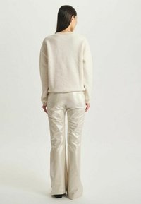 Pull crème avec une coupe décontractée, associé à un pantalon flare beige clair métallisé, mettant en avant une texture lisse et une couture simple.