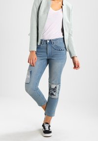 Světle modré džíny s cropped délkou, zdobené dekorativními nášivkami, vyšívaným designem a volným střihem. Nosit s bílou košilí a bundou.