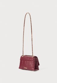 Sac à main en cuir bordeaux avec un design matelassé, une bandoulière en chaîne dorée et un panneau texturé contrastant. Dispose d'une fermeture à rabat magnétique.
