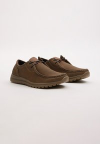 Zapatillas de cuero marrón con puntera redondeada, costuras decorativas, cordones y una suela de goma con un patrón de agarre texturizado.
