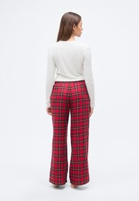 Λευκό μακρυμάνικο τοπ σε συνδυασμό με κόκκινο και μαύρο καρό παντελόνι με φαρδιά μπατζάκια. Το παντελόνι διαθέτει ελαστική μέση και απαλό ύφασμα.