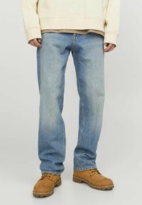 Light blue denim jeans with a relaxed fit, worn with a cream-colored sweatshirt, and brown ankle boots featuring laces and a rugged sole.