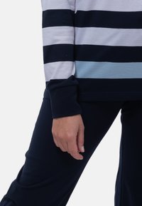 Granatowa i jasnoniebieska w paski bluzka z długim rękawem z podwiniętymi mankietami, w połączeniu z ciemnoniebieskimi spodniami. Miękki materiał o luźnym kroju.