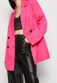 Rosa oversize blazer med en texturerad yta, som har två svarta knappar och en frampocket, ihop med svarta läderbyxor.