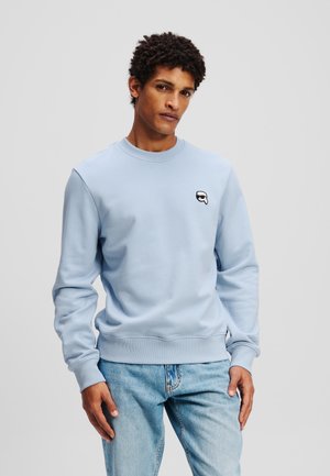 Hellblaues Sweatshirt aus weichem Stoff, mit Rundhalsausschnitt und gerippten Bündchen, versehen mit einem kleinen schwarz-weißen Logo auf der Brust.