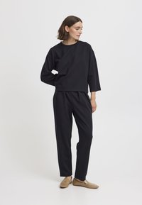 Felpa nera, leggera e corta con una vestibilità rilassata, abbinata a pantaloni neri su misura con frontale plissettato e caviglie risvoltate.