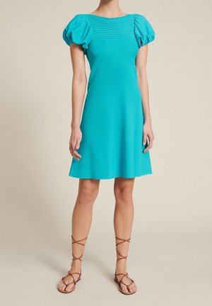 Türkisfarbenes Kleid mit kurzen Puffärmeln, strukturierter Taille und ausgestelltem Rock. Kombiniert mit braunen Riemchensandalen. Glatte Stoffstruktur.