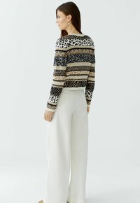 Strickpullover mit gestreiftem Muster in Schwarz, Beige und Braun sowie Tiermotiven. Kombiniert mit weiten weißen Hosen.