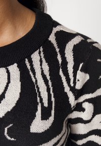 Gros plan d’un pull noir et blanc avec un motif audacieux et abstrait de rayures de zèbre et un col rond côtelé.