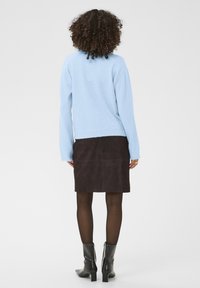 Pull en maille bleu clair à manches longues, associé à une jupe en suède marron, des collants opaques noirs et des bottines noires.