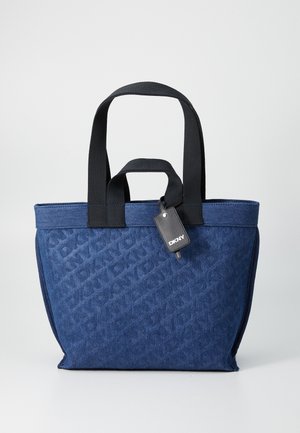 Mørkeblå totebag med et strukturert stoff, som har svarte håndtak og en DKNY-lapp. Vesken har en strukturert form og et diskret logomønster.