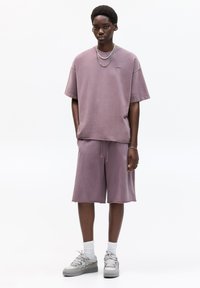 Aansluitend lavendelkleurig katoenen T-shirt met korte mouwen, gecombineerd met bijpassende drawstring shorts. Ggedragen met grijze sneakers en witte sokken.
