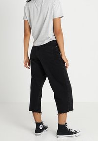 Jeans negros recortados con dobladillo deshilachado, combinados con una camiseta gris y zapatillas de caña alta negras. La tela parece vaquera con una textura suave.