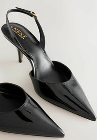 Melni lakotas ādas augstpapēžu apavi ar atvērtu papēdi, asiem purngaliem un plānu stiletto papēdi. Ap potīti ir sudraba piespraude zelta tonī.