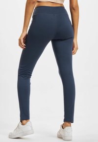 Marineblauwe legging met een slim fit en brede tailleband, gemaakt van soepel, rekbaar materiaal. Gecombineerd met witte sneakers.
