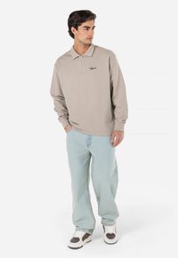 Lysegrå langærmet polo med lynlås foran, broderi på brystet, kombineret med lyseblå baggy jeans og hvide sneakers.