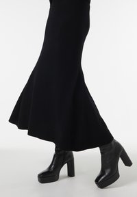 Robe en tricot noire avec ourlet évasé, associée à des bottines à plateforme en cuir noir avec un bout carré et un talon épais.
