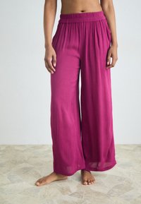Fuchsia wide-leg pants with a pleated texture, elastic waistband, and side pockets. Lightweight fabric, suitable for casual wear.