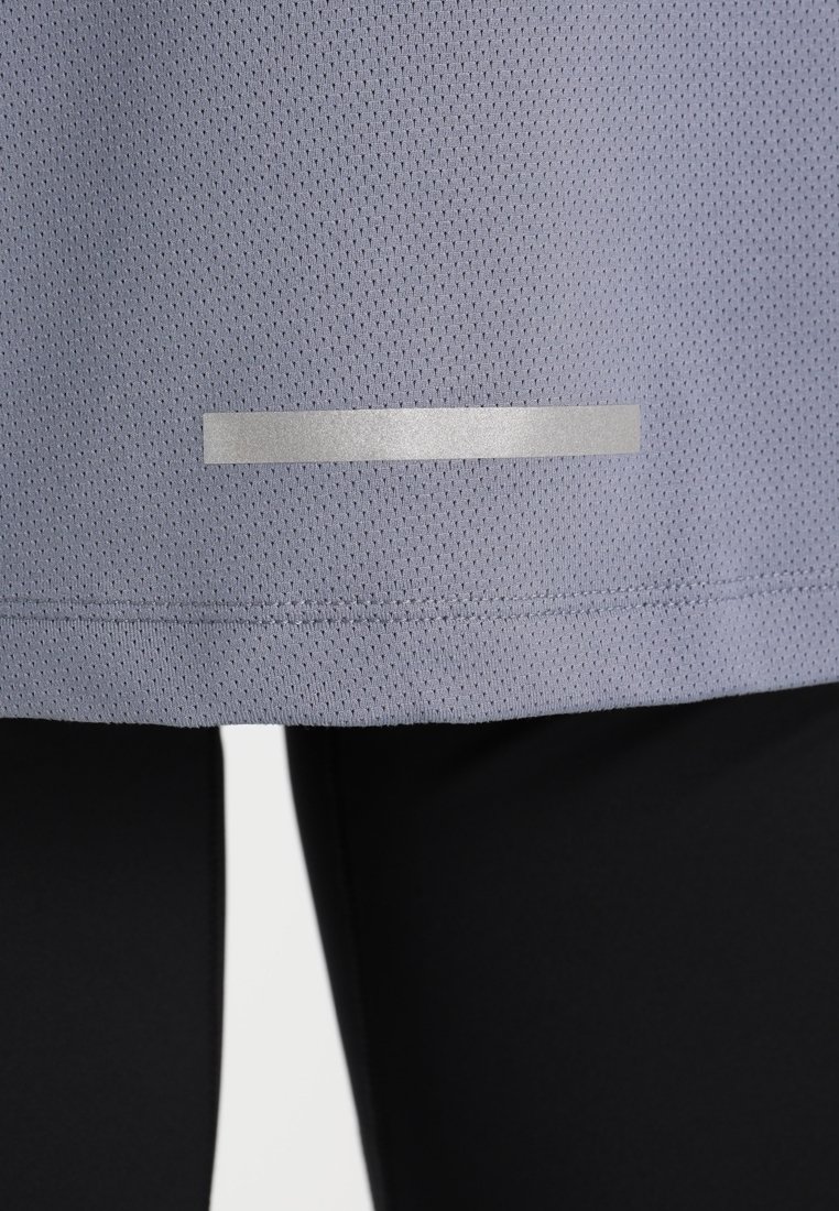 Ljuslila sporttopp med ett strukturerat, ventilerande tyg. Har en silverreflekterande remsa vid fållen för ökad synlighet.