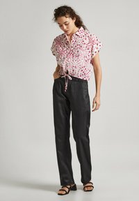 Blusa de botón de manga corta con un patrón geométrico en rosa y blanco, combinada con pantalones negros de corte holgado y sandalias de tiras.