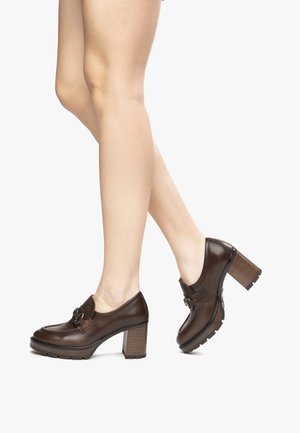 Scarpe con tacco in pelle marrone con punta arrotondata, dotate di una fibbia decorativa e un tacco squadrato texturizzato. Suola in gomma per una presa sicura.