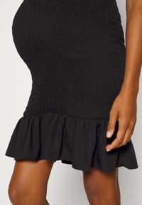 Vestido preto com um design simples, com franzidos texturizados e uma bainha em babados. O tecido parece suave, com um leve brilho.