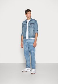 Lyseblå denimjakke og matchende jeans med en hvid t-shirt. Lærredssneakers har hvide og brune detaljer. Simpelt, afslappet design.