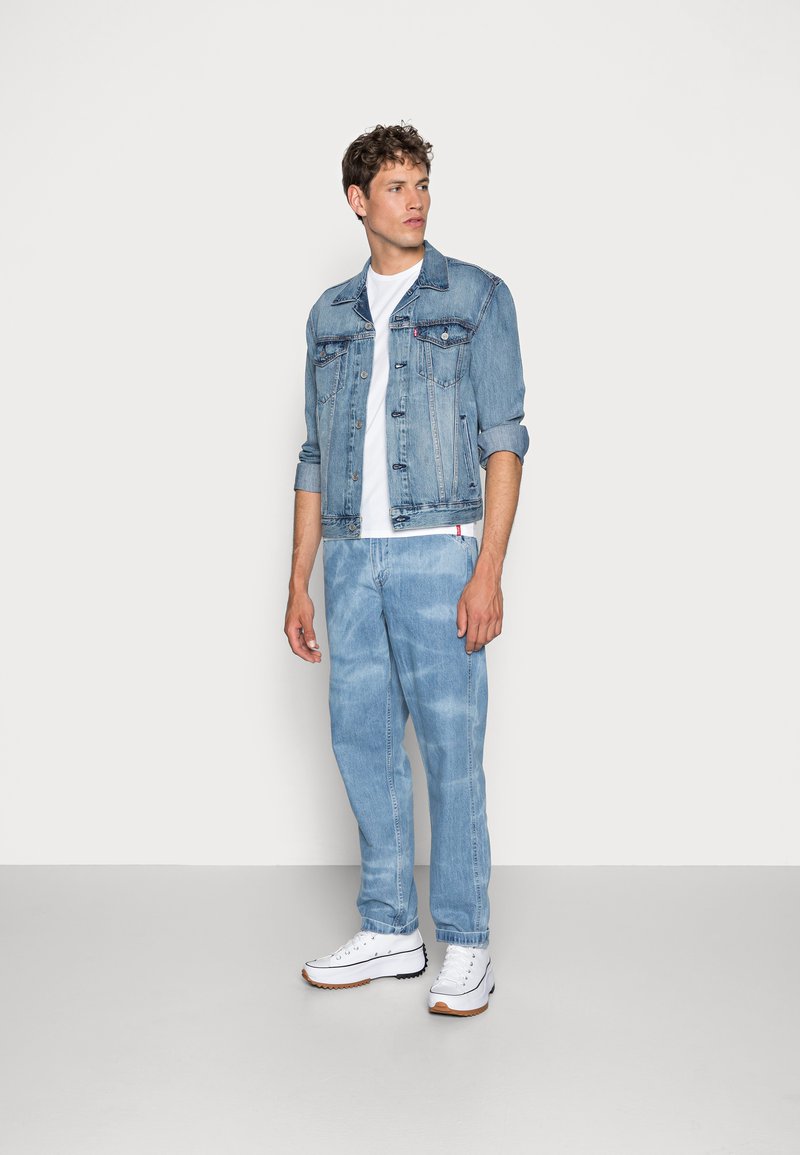 Lyseblå denimjakke og matchende jeans med en hvid t-shirt. Lærredssneakers har hvide og brune detaljer. Simpelt, afslappet design.